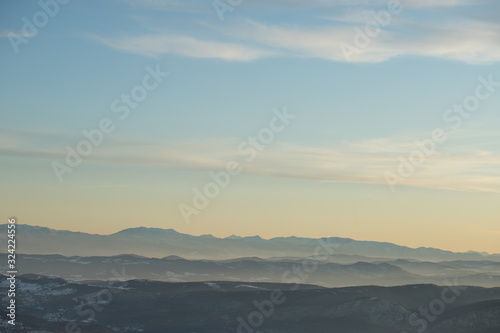 Beautiful view of the mountain range partially covered with snow just before sunset. Partly orange sunset sky