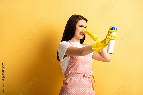 Φωτογραφία displeased housewife in apron and rubber gloves plugging hose with hand while sp