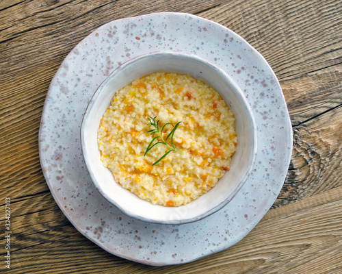 millet porridge with grated pumpkin in a bowl on wooden background