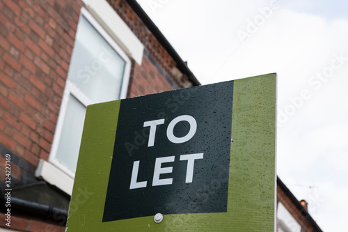 UK United Kingdom green lettings To Let rental property sign with red brick house in background. Landlord investment property portfolio real estate British England concept idea