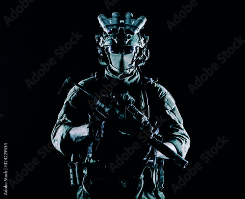 Army elite soldier with hidden behind mask and glasses face, in full tactical ammunition, equipped night vision device, radio headset, armed short barrel service rifle studio contour shot photo