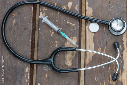 A close up view of a medical stethoscope next to a saringe and needle. On a wooden table