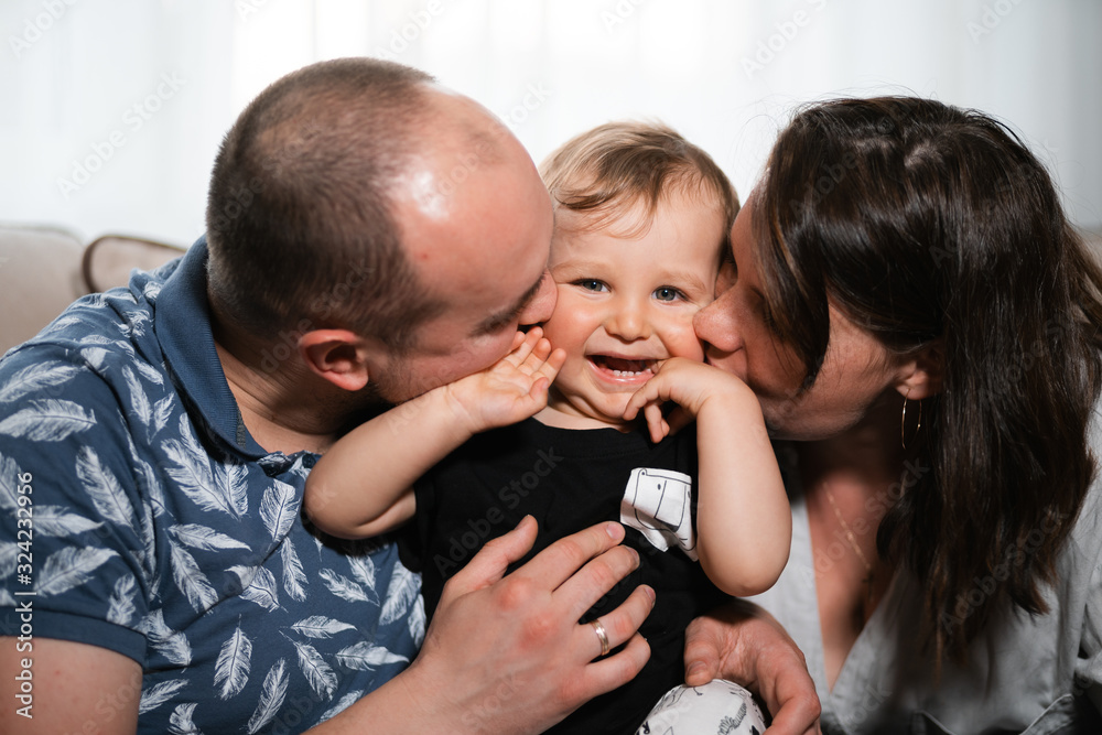 Family values: Mother and father playing with baby child boy indoor - Parents wearing blue and gray home wear and their son black and white - Happy smiling people Family values: Mother and father playing with baby child boy indoor - Parents wearing blue and gray home wear and their son black and white - Happy smiling people