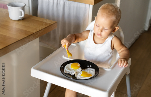 Obraz na plátně A small child independently eats a fried egg with a fork