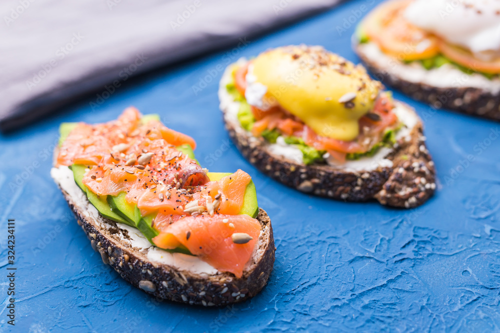 Sandwiches with smoked salmon, eggs, sauce and avocado on blue background. Concept of breakfast and healthy nutrition.