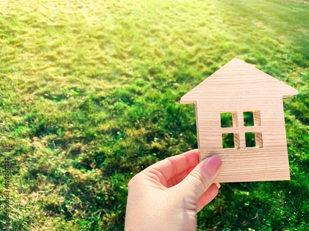 Miniature wooden house on green grass in female hands. Real estate concept. Modern housing. Eco-friendly and energy efficient house. Buying a home outside the city. Nature. Fresh air. Mortgage, loan. Miniature wooden house on green grass in female hands. Real estate concept. Modern housing. Eco-friendly and energy efficient house. Buying a home outside the city. Nature. Fresh air. Mortgage, loan.