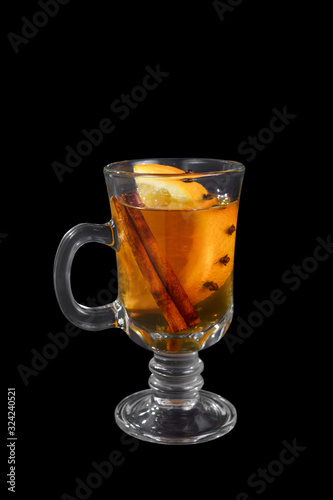 Monochrome transparent cocktail, orange mulled wine in a high glass with a handle with spices and a slice of lemon, orange, side view, iIsolated black background. Drink for the menu restaurant, bar