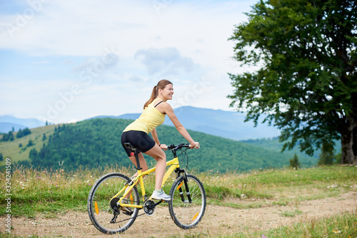 Athlete happy woman cyclist cycling on yellow mountain bike, enjoying summer day in the mountains. Outdoor sport activity, lifestyle concept