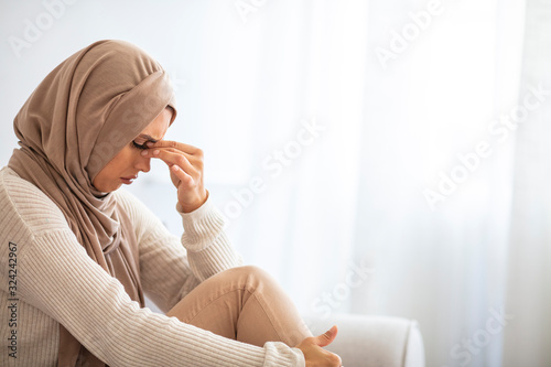 Sinus pain, sinus pressure, sinusitis. Sad Muslim woman holding her nose and head because sinus pain. Sinus ache causing very paintful headache. Unhealthy woman in pain. Sharp strong sore photo