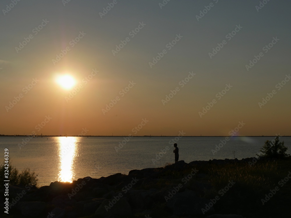 Scenic sunset by the lake, with the silhouette of a man on the rocky shoreline.