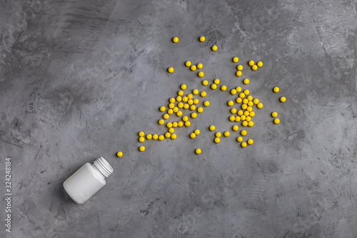 Yellow vitamins poured from a white can on a gray concrete background.