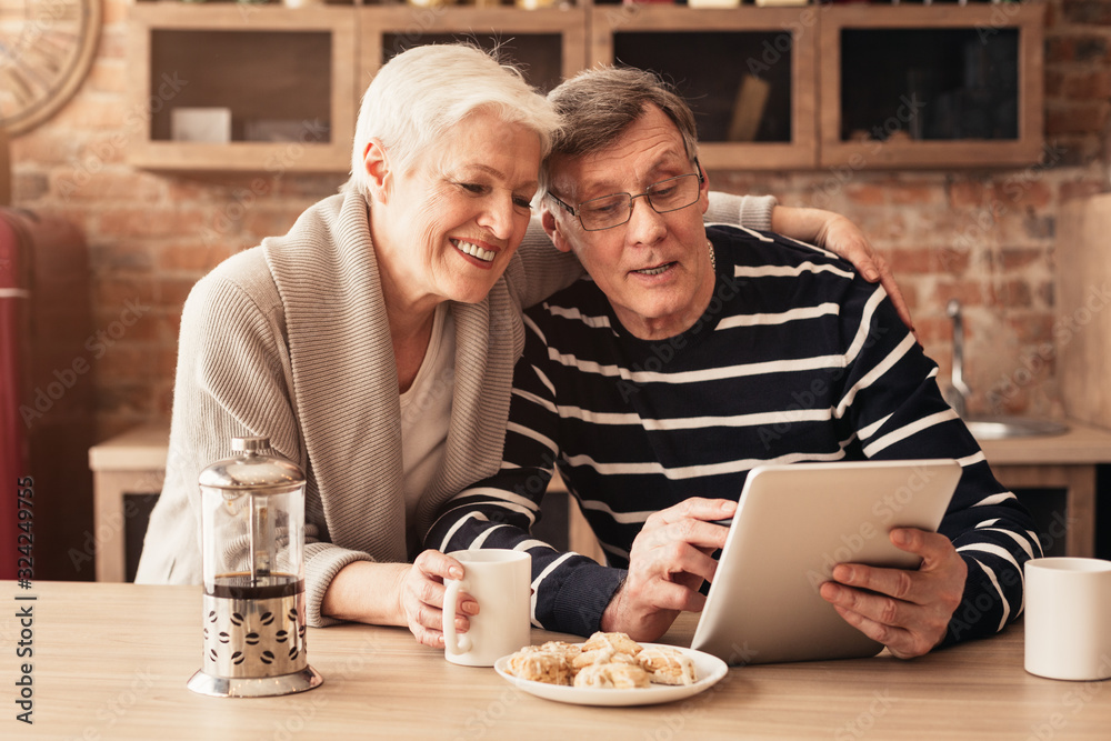 Happy Senior Couple Using Digital Tablet And Drinking Coffee In Kitchen Happy Senior Couple Using Digital Tablet And Drinking Coffee In Kitchen