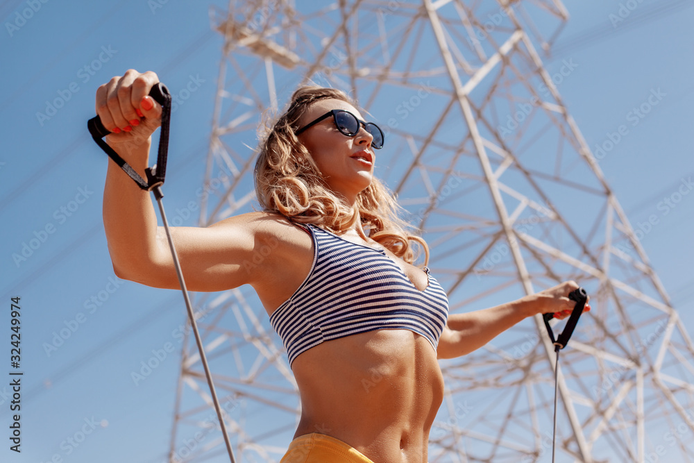 Sexy athletic girl in sunglasses trains with an expander against the sky .  Sports, fitness, healthy lifestyle Stock Photo | Adobe Stock