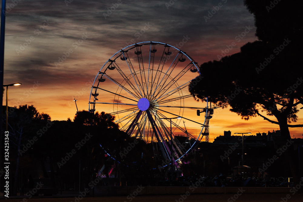 Colorful sky and Ferris wheel. Sunset through a Ferris Wheel in Antibes, France.Silhouette of giant ferris wheel on sunset. Illuminated Ferris wheel at sunset. 