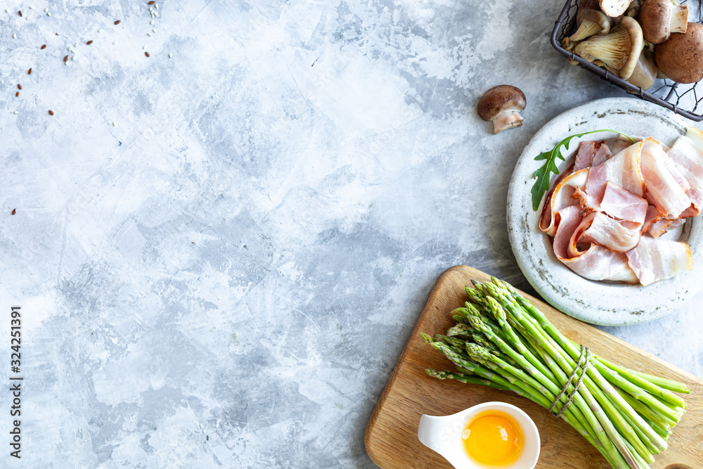 Ingredients for cooking on a gray concrete background. A bunch of fresh green asparagus, eggs, bacon, mushrooms. Top view. Copy space Ingredients for cooking on a gray concrete background. A bunch of fresh green asparagus, eggs, bacon, mushrooms. Top view. Copy space
