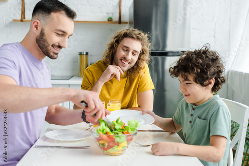 happy homosexual men and mixed race kid looking at tasty salad