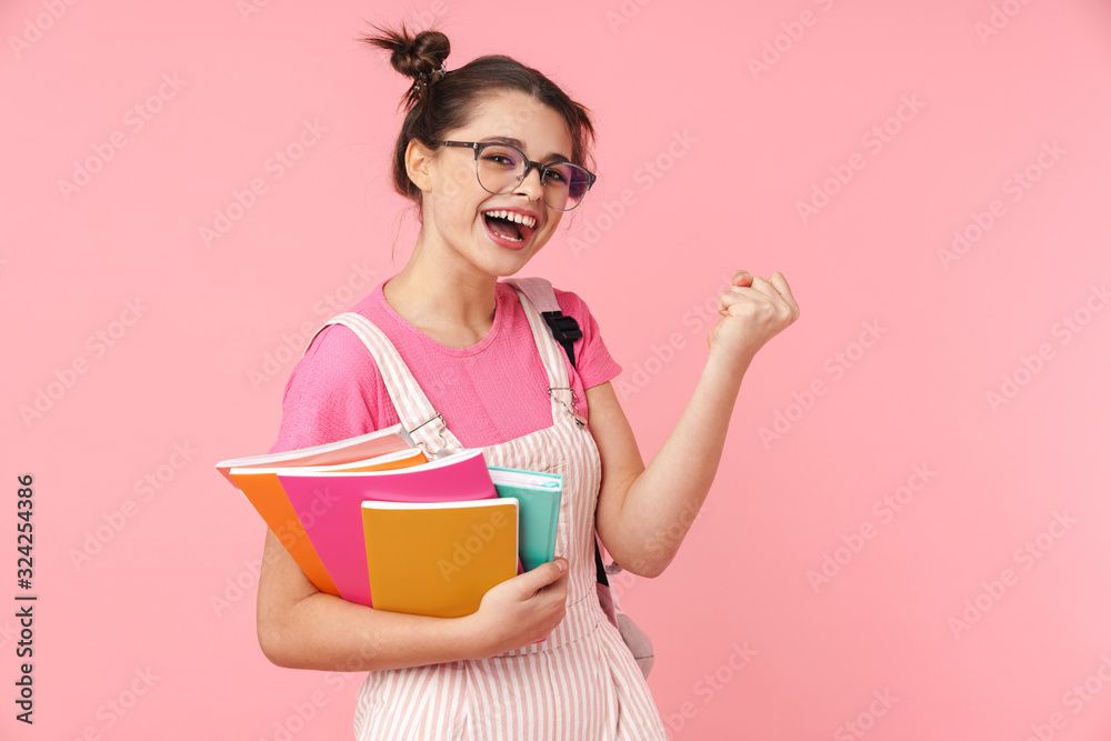 Photo of delighted girl holding exercise books and making winner gesture Photo of delighted girl holding exercise books and making winner gesture
