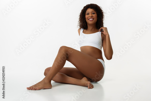 Posing confident, love herself. Slim tanned woman's on white studio background. African-american model with well-kept shape and skin. Beauty, self-care, fitness, slimming concept. Healthcare. © master1305