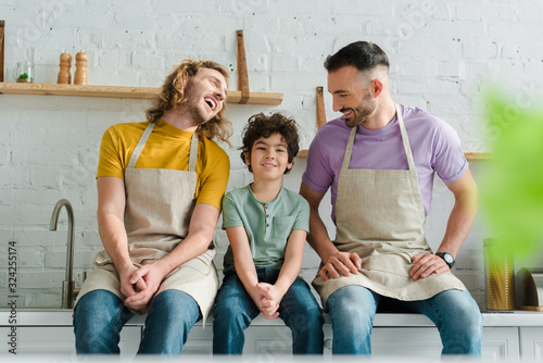 selective focus of happy homosexual parents smiling with mixed race son