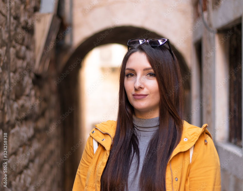 Attractive brunette standing in a public narrow street in split, croatia. Wearing a yellow jacket smiling, fashionable youth