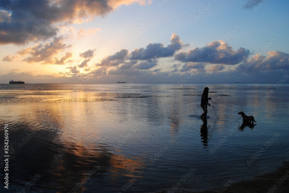 Beautiful sunset in the Northern Mariana Islands with the silhoutte of a woman and a dog in the beach
