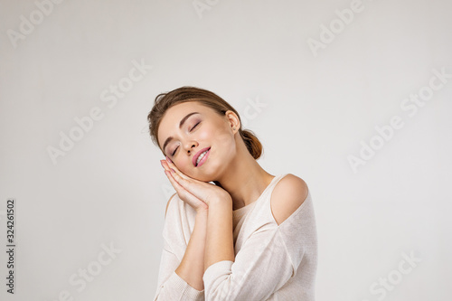 Portrait of young beautiful woman is showing sleep gesture on gray background