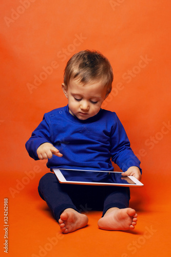 A pretty toddler boy imitates a work on the tablet computer. Trending colors of clothing and background. The concept of early use of gadgets, the theme of children and electronics.