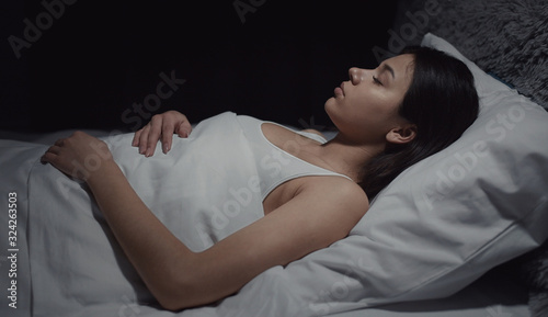 Portrait of brunette in nightwear lying on back sleeping covered in bed, half-body pic, side view
