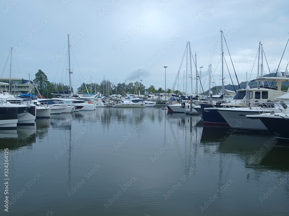 Yachts moored in the sea bay. Panoramic view of sailing yachts anchored in the sea lagoon. Sports yacht club. Green hills on the horizon, reflection of the sides of the yachts on the surface of water
