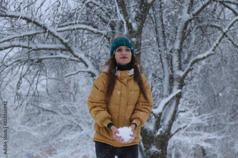 Beautiful girl in a yellow jacket, jeans and a green hat on the snow. Snowy weather, everything in the snow is white. Snowflakes.