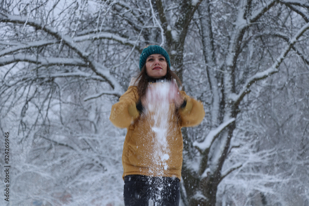 Fototapeta premium Beautiful girl in a yellow jacket, jeans and a green hat on the snow. Snowy weather, everything in the snow is white. Snowflakes.