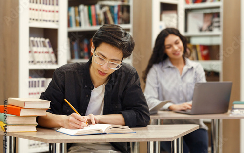 Asian guy doing research sitting at desk in library