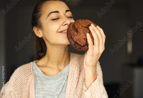 pretty smiling woman holding and sniffing huge chocolate cookie with pleasure. food, sweets and bakery concept.