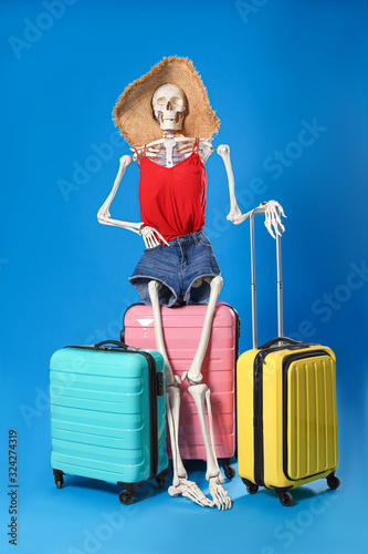 Fotografie Human skeleton in summer clothes with suitcases on blue background