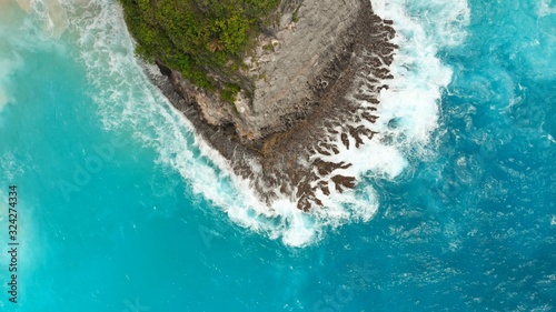 White-blue waves beat on the rocks of the island of Nusa Penida near Kelingking beach.