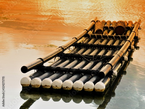 Bamboo raft floating in a shallow part of the beach with the colors of sunset reflected in the water photo