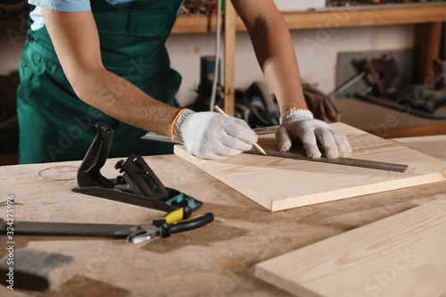 Professional carpenter measuring wooden board in workshop, closeup photo