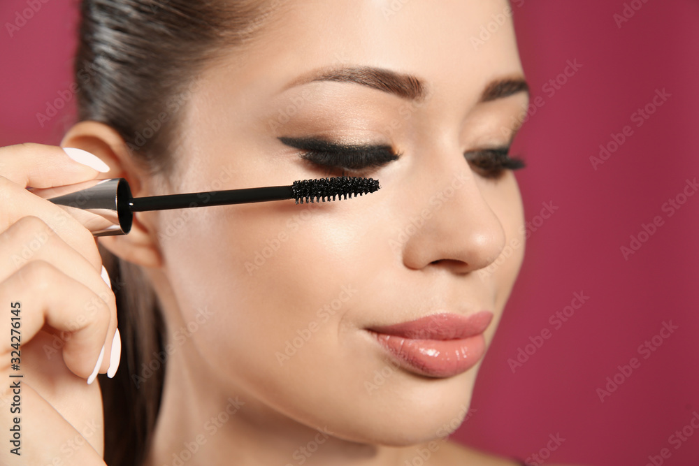 Beautiful woman applying mascara on pink background, closeup. Stylish makeup