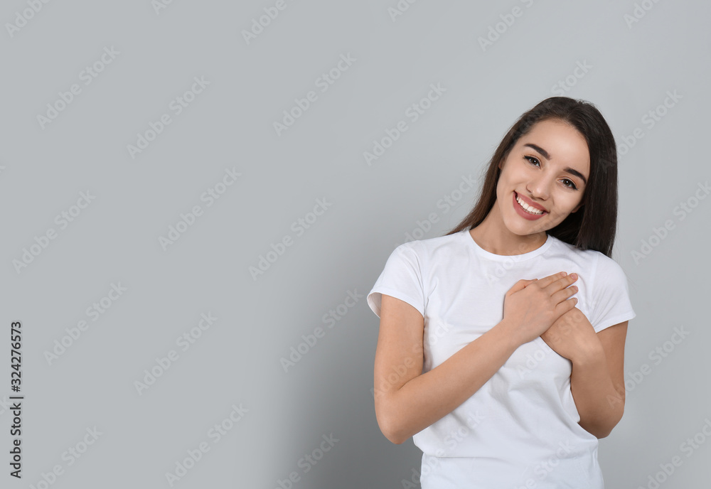 Beautiful grateful woman with hands on chest against light grey background. Space for text Beautiful grateful woman with hands on chest against light grey background. Space for text