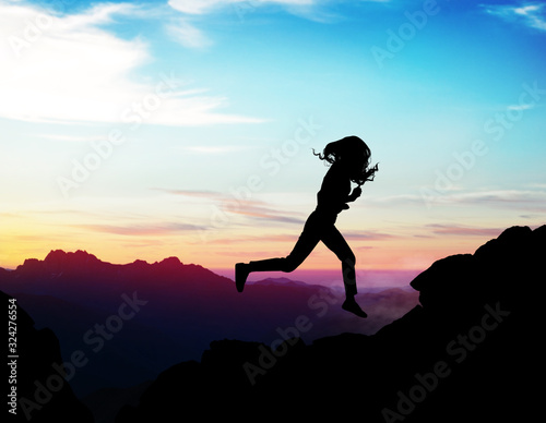 Black silhouette of woman running forward on the rock.