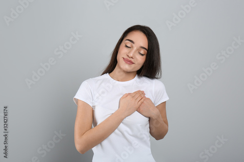 Beautiful grateful woman with hands on chest against light grey background