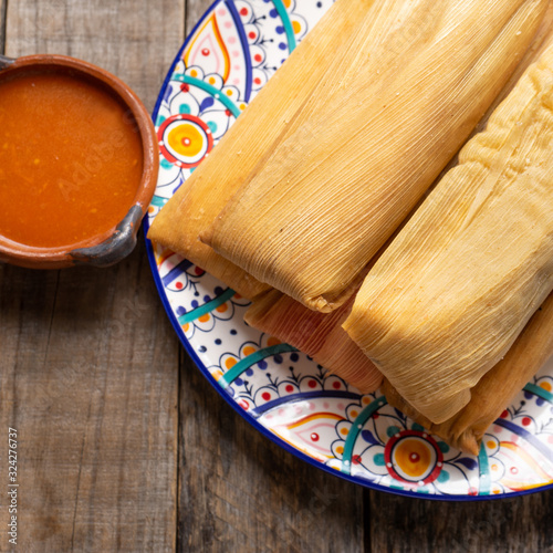 Mexican tamales with red sauce on wooden background