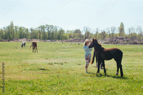 . Spring, trees are blooming, grass is growing . .woman walks on a background of a horse. .woman stroking a horse © younnona