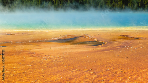 Steam rising from thr Grand Prismatic Spring in Yellowstone National Park with bright orange bacteria and blue water
