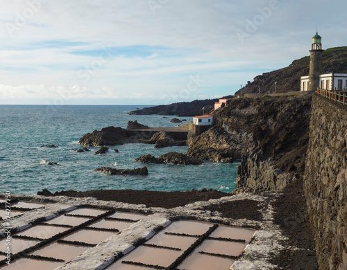 View of Fuencaliente salinas or saltworks and old stone lighthouse with volcanic rock field. La Palma, Canary Islands. Ocean, blue sky white clouds.
