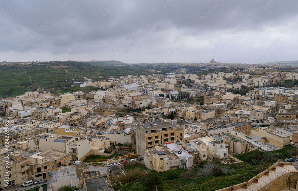 The outskirts of the destroyed European city on the island of Gozo, in the frame the houses and streets near green hill.