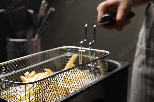 Chef cooking delicious french fries in hot oil, closeup