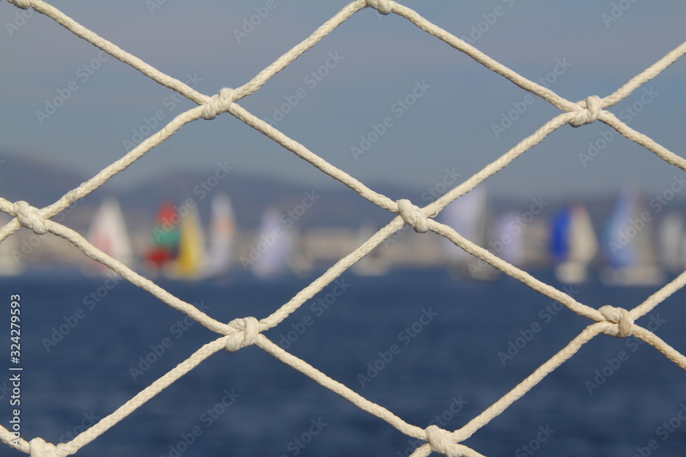 Detail image of wooden pulley with ropes of an classical sailing yacht. ocean and sailing boats in the blurry background Detail image of wooden pulley with ropes of an classical sailing yacht. ocean and sailing boats in the blurry background