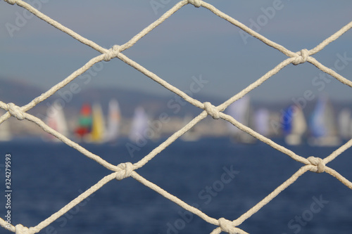 Detail image of wooden pulley with ropes of an classical sailing yacht. ocean and sailing boats in the blurry background