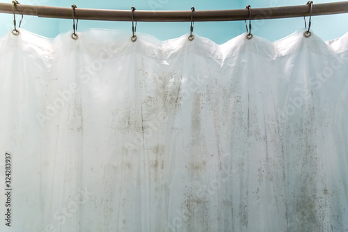 Dark brown mildew mold on plastic interior shower curtain in a light aqua bathroom